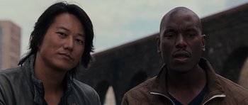 Movie still from “Fast & Furious 6” (2013), directed by Justin Lin – A man and a woman standing next to each other in front of a bridge; Close Up shot, Low angle