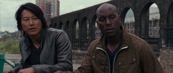 Movie still from “Fast & Furious 6” (2013), directed by Justin Lin – A man in brown jacket sitting next to another man in a brown jacket; Close Up shot, Over the shoulder angle