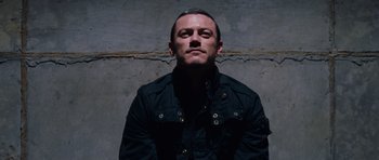 Movie still from “Fast & Furious 6” (2013), directed by Justin Lin – A man wearing a black jacket standing in front of a wall; Medium shot, Overhead angle