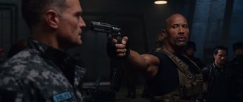 Movie still from “Fast & Furious 6” (2013), directed by Justin Lin – A man holding a gun pointed at another man; Medium shot, Over the shoulder angle