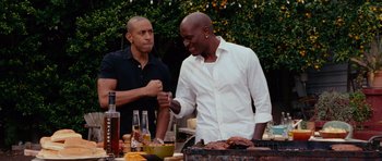 Movie still from “Fast & Furious 6” (2013), directed by Justin Lin – Two men standing at a table preparing food on top of a grill; Medium shot, Low angle