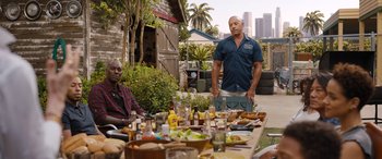 Movie still from “Fast X” (2023), directed by Justin Lin – A man standing next to another man at an outdoor table; Medium shot, Over the shoulder angle