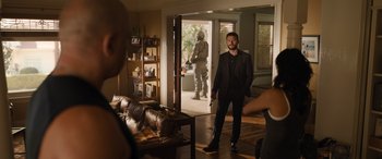 Movie still from “Fast X” (2023), directed by Justin Lin – A man in a black suit is holding a gun; Wide shot, Over the shoulder angle