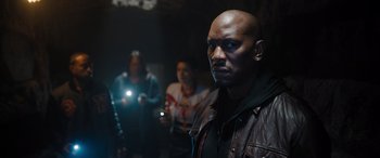 Movie still from “Fast X” (2023), directed by Justin Lin – A group of people standing in a dark room; Medium shot, Over the shoulder angle