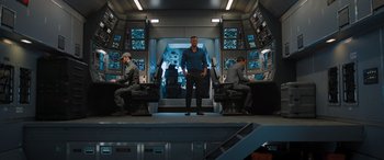 Movie still from “Fast X” (2023), directed by Justin Lin – A man standing in front of two other men in a room; Wide shot, Over the shoulder angle