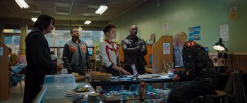 Movie still from “Fast X” (2023), directed by Justin Lin – A group of people standing around a table in a store; Medium shot, Over the shoulder angle