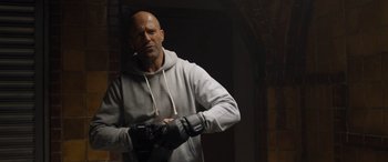 Movie still from “Fast X” (2023), directed by Justin Lin – A bald man in a gray hoodie is holding a pair of gloves; Medium shot, Low angle
