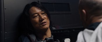 Movie still from “Fast X” (2023), directed by Justin Lin – A man with long black hair is holding a gun; Close Up shot, Over the shoulder angle