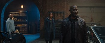 Movie still from “Fast X” (2023), directed by Justin Lin – Two people standing next to each other near a brick wall; Medium shot, Over the shoulder angle