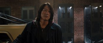 Movie still from “Fast X” (2023), directed by Justin Lin – A man with long black hair wearing a black jacket; Close Up shot, Over the shoulder angle