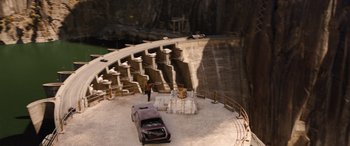 Movie still from “Fast X” (2023), directed by Justin Lin – An aerial view of a man standing next to a car in front of a dam; Extreme Wide shot, High angle