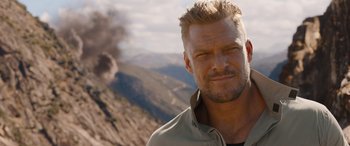 Movie still from “Fast X” (2023), directed by Justin Lin – A person wearing a jacket near a mountain; Close Up shot, Over the shoulder angle