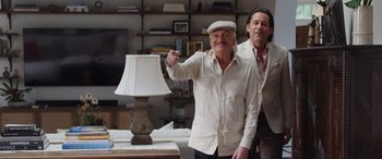 Movie still from “Father of the Bride” (2022), directed by Gary Alazraki – Two men standing in front of a lamp in a living room; Wide shot, Low angle