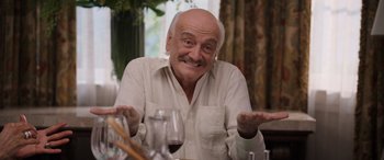 Movie still from “Father of the Bride” (2022), directed by Gary Alazraki – An older man sitting at a table with a glass of red wine; Medium shot, Low angle