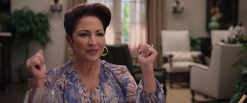 Movie still from “Father of the Bride” (2022), directed by Gary Alazraki – An older woman in a blue floral shirt holding a cigarette; Close Up shot, Over the shoulder angle