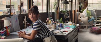 Movie still from “Father of the Bride” (2022), directed by Gary Alazraki – A woman sitting at a table in front of a painting; Medium shot, Over the shoulder angle