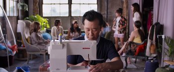 Movie still from “Father of the Bride” (2022), directed by Gary Alazraki – A man sitting in front of a white sewing machine; Medium shot, Over the shoulder angle