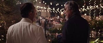 Movie still from “Father of the Bride” (2022), directed by Gary Alazraki – A man smoking a cigar while talking to another man in a suit; Medium shot, Over the shoulder angle
