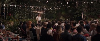 Movie still from “Father of the Bride” (2022), directed by Gary Alazraki – A group of people sitting at tables and a man standing at a microphone; Wide shot, Over the shoulder angle