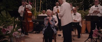 Movie still from “Father of the Bride” (2022), directed by Gary Alazraki – An older woman sitting in a chair with a microphone; Medium shot, Over the shoulder angle