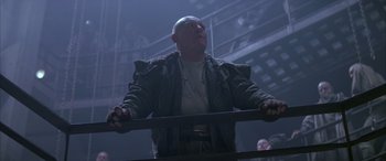 Movie still from “Alien³” (1992), directed by David Fincher – A bald man in a leather jacket stands in a dark room; Medium shot, Low angle