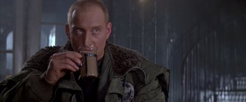 Movie still from “Alien³” (1992), directed by David Fincher – A man drinking from a mug while wearing a jacket; Close Up shot, Over the shoulder angle
