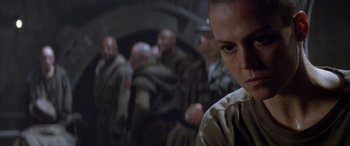 Movie still from “Alien³” (1992), directed by David Fincher – A group of people in a dark room with one person looking at the camera; Close Up shot, Low angle