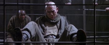 Movie still from “Alien³” (1992), directed by David Fincher – A man sitting on a chair in front of a fence; Medium shot, Low angle