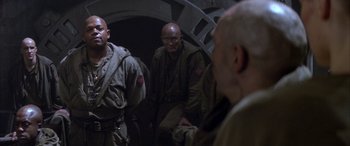 Movie still from “Alien³” (1992), directed by David Fincher – A group of men standing next to each other in a room; Medium shot, Over the shoulder angle