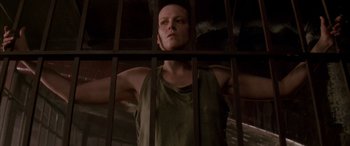 Movie still from “Alien³” (1992), directed by David Fincher – A man standing behind bars in a jail cell; Medium shot, Low angle