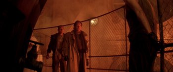Movie still from “Alien³” (1992), directed by David Fincher – Two men standing next to each other near a chain link fence; Wide shot, Low angle