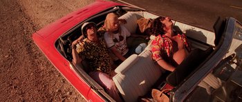 Movie still from “Fear and Loathing in Las Vegas” (1998), directed by Terry Gilliam – A group of people in the back of a red car; Wide shot, High angle