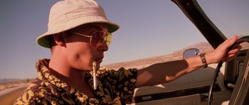 Movie still from “Fear and Loathing in Las Vegas” (1998), directed by Terry Gilliam – A man with a hat and sunglasses is driving a car and holding a cigarette; Close Up shot, Low angle