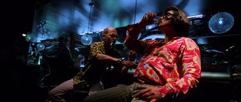 Movie still from “Fear and Loathing in Las Vegas” (1998), directed by Terry Gilliam – Two men are sitting in a bar and one of them is drinking a beverage; Medium shot, Low angle