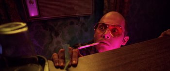 Movie still from “Fear and Loathing in Las Vegas” (1998), directed by Terry Gilliam – A bald man with glasses is smoking a cigarette; Close Up shot, Low angle