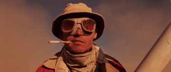 Movie still from “Fear and Loathing in Las Vegas” (1998), directed by Terry Gilliam – A man wearing a hat and sunglasses while holding a cigarette in his mouth; Close Up shot, Low angle