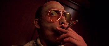 Movie still from “Fear and Loathing in Las Vegas” (1998), directed by Terry Gilliam – A man with a cigarette in his mouth and sunglasses on; Close Up shot, Low angle