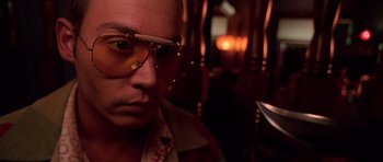 Movie still from “Fear and Loathing in Las Vegas” (1998), directed by Terry Gilliam – A man wearing glasses and a yellow shirt is looking at the camera; Close Up shot, Low angle