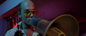 Movie still from “Fear and Loathing in Las Vegas” (1998), directed by Terry Gilliam – A bald man wearing sunglasses is blowing into a trumpet; Close Up shot, Low angle
