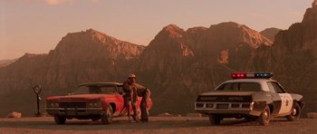 Movie still from “Fear and Loathing in Las Vegas” (1998), directed by Terry Gilliam – A man standing next to a red car in front of mountains; Wide shot, Low angle