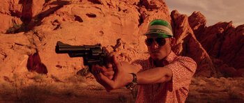 Movie still from “Fear and Loathing in Las Vegas” (1998), directed by Terry Gilliam – A man holding a gun while standing in front of a rock wall; Medium shot, Low angle