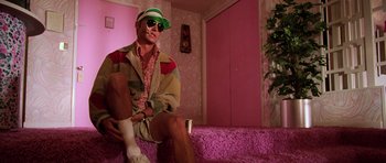 Movie still from “Fear and Loathing in Las Vegas” (1998), directed by Terry Gilliam – A man sitting on a couch wearing a green hat; Medium shot, Low angle