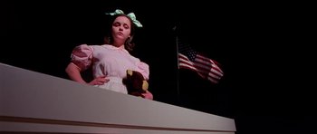 Movie still from “Fear and Loathing in Las Vegas” (1998), directed by Terry Gilliam – A girl in a pink dress holding a teddy bear in front of an american flag; Medium shot, Low angle