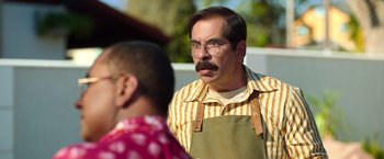 An older man with a mustache and glasses is standing next to another man