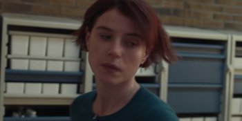 Movie still from “Fingernails” (2023), directed by Christos Nikou – A woman with red hair is standing in front of a book shelf; Close Up shot, Over the shoulder angle