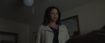 Movie still from “Firestarter” (2022), directed by Keith Thomas – A woman standing in front of a painting in a dark room; Medium shot, Low angle