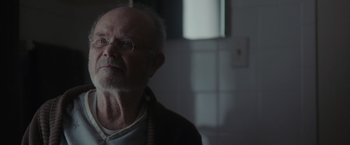 Movie still from “Firestarter” (2022), directed by Keith Thomas – An old man with a beard and glasses looking into the distance; Close Up shot, Over the shoulder angle