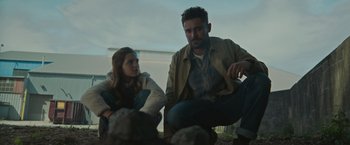 Movie still from “Firestarter” (2022), directed by Keith Thomas – A man and a woman sitting next to each other on the ground; Medium shot, Low angle