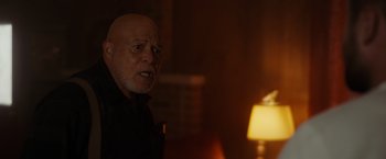 Movie still from “Firestarter” (2022), directed by Keith Thomas – An older man is standing in a dimly - lit room; Medium shot, Over the shoulder angle
