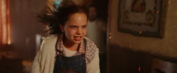 Movie still from “Firestarter” (2022), directed by Keith Thomas – A young girl is smiling while wearing an apron; Close Up shot, Low angle